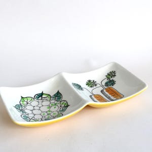 Puede incluir: Un plato dividido de cerámica blanca con un borde amarillo. Un lado presenta un diseño floral verde y blanco, mientras que el otro lado tiene un diseño de zanahoria verde y naranja.