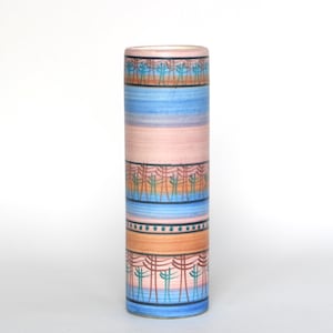 May include: A cylindrical ceramic vase with a colorful, layered design. The vase features bands of blue, pink, and orange, each adorned with a stylized tree pattern. The overall aesthetic is reminiscent of a desert landscape.