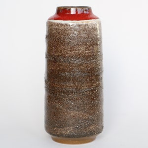 Puede incluir: Un jarrón de cerámica marrón con un borde rojo y un esmalte moteado. El jarrón tiene una forma cilíndrica y mide aproximadamente 25 cm de alto.