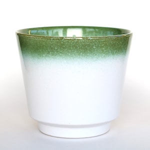 Op de afbeelding: Een witte keramische plantenpot met een groen ombre-effect op de bovenrand. De pot heeft een cilindrische vorm met een licht uitlopende bovenkant en een kleine, verhoogde basis. De binnenkant is groen.