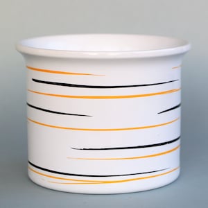 Op de afbeelding: Witte keramische mok met zwarte en oranje strepen.