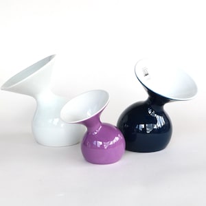 Op de afbeelding: Drie keramische vazen in wit, paars en marineblauw. Elke vaas heeft een afgeronde basis en een brede, schuine opening. De vazen zijn gerangschikt op een wit oppervlak, wat hun glanzende afwerking en unieke ontwerp laat zien.