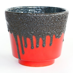 Op de afbeelding: Een rode keramische plantenpot met een getextureerde, donkergrijze band rond de rand. Het donkergrijze materiaal druipt langs de zijkanten. De pot heeft een kleine, ronde basis.