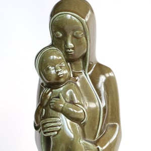 Peut inclure: Une sculpture en céramique de la Vierge Marie tenant un bébé Jésus. La sculpture est peinte dans des tons de vert et de brun.