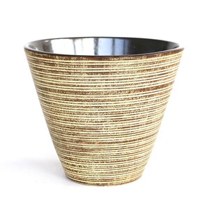 Op de afbeelding: Een decoratieve keramische vaas met een brede, uitlopende vorm. De buitenkant heeft horizontale strepen in beige en bruine tinten. De binnenkant is donkerbruin, wat een contrast creëert. De vaas staat tegen een witte achtergrond.