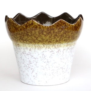 May include: A ceramic flower pot with a scalloped rim. The pot has a speckled white base, transitioning to a yellow-brown midsection, and a dark brown rim. A decorative piece for home decor.