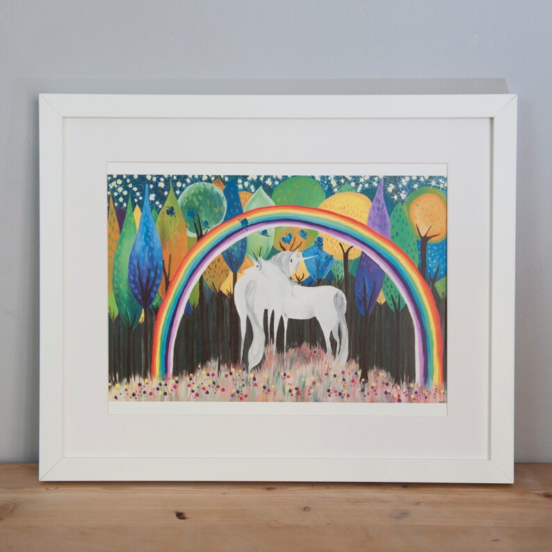 May include: A framed illustration of two white unicorns standing in a forest with a rainbow arching over them. The forest is filled with colorful trees and flowers. The background is a dark blue sky with white stars.