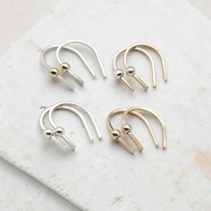 May include: Four pairs of U-shaped ear cuffs in silver and gold tones. Each cuff features a smooth, curved wire design with a small spherical bead accent at one end. The collection includes two pairs with silver-toned beads and two pairs with gold-toned beads.