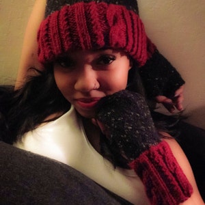 May include: A woman wearing a red and black knit hat and matching fingerless gloves. The hat has a cable knit pattern and the gloves have a speckled pattern.