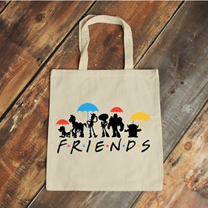 May include: Cream canvas tote bag with a graphic of cartoon character silhouettes under coloured umbrellas. The word "FRIENDS" is printed in black, with each letter in a different colour.