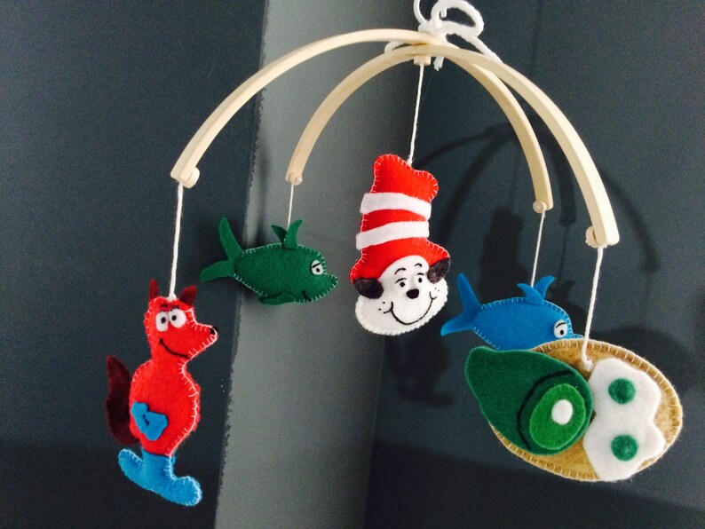 K&ouml;nnte beinhalten: Ein Holz-Babymobil mit Filztieren und Fischfiguren. Die Figuren umfassen einen roten Fisch, einen gr&uuml;nen Fisch, einen blauen Fisch und eine rote Katze mit Hut.