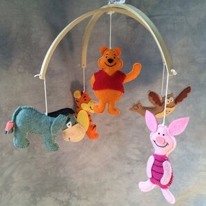 K&ouml;nnte beinhalten: Ein Holz-Babymobil mit Filzfiguren aus Winnie Puuh. Das Mobile zeigt Winnie Puuh, Ferkel, Esel, Tiger und eine Eule.