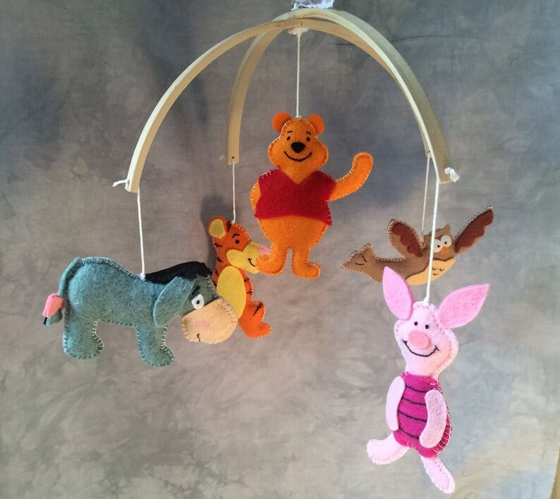 K&ouml;nnte beinhalten: Ein Holz-Babymobil mit Filzfiguren aus Winnie Puuh. Das Mobile zeigt Winnie Puuh, Ferkel, Esel, Tiger und eine Eule.