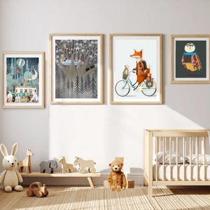May include: Four framed wall art prints featuring whimsical animal illustrations, including a fox on a bicycle, a forest scene with a camper, a tree with animals, and a colorful owl, displayed above a wooden crib and a low shelf with wooden toys.