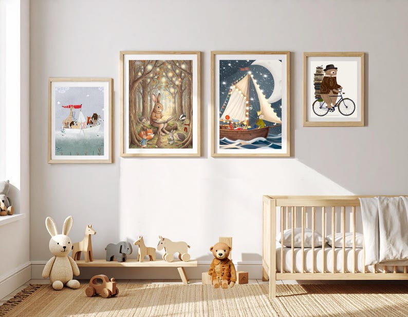May include: Four framed wall art prints featuring whimsical animal illustrations, including a boat with animals, a rabbit reading in a forest, a sailboat under a crescent moon, and a bear riding a bicycle, displayed above a wooden crib and toys.