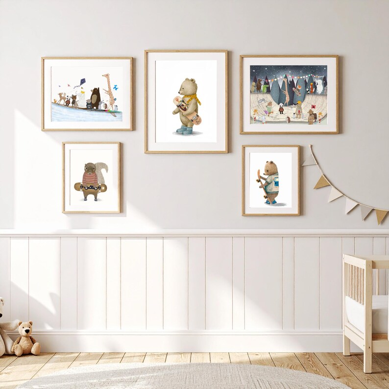 May include: A gallery wall set of five framed art prints featuring illustrations of animals, including bears and a squirrel, with some holding skateboards. The prints are displayed in light wood frames against a plain wall above a white wainscot.