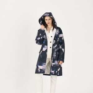Puede incluir: Una chaqueta larga con capucha de color negro y blanco con estampado, con una cremallera blanca y un cuello blanco. La chaqueta se lleva sobre una camisa blanca abotonada y unos pantalones blancos.