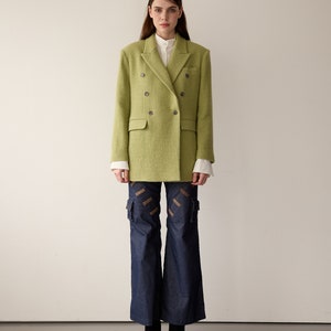 May include: A green double-breasted blazer with a white collared shirt underneath. The blazer has a textured fabric and is worn with blue denim pants.