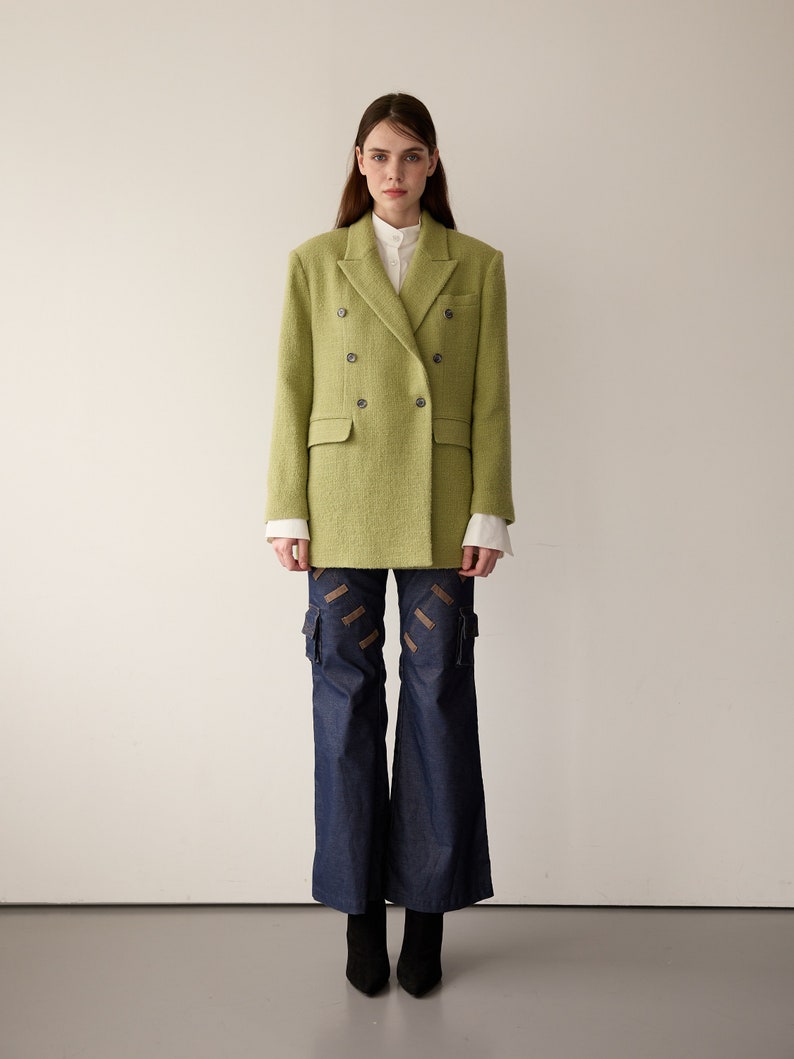 May include: A green double-breasted blazer with a white collared shirt underneath. The blazer has a textured fabric and is worn with blue denim pants.