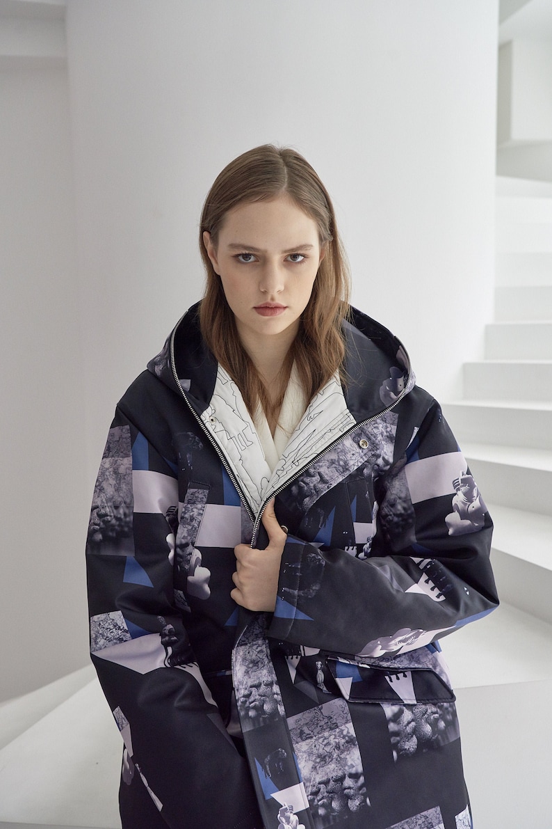 Puede incluir: Una chaqueta negra con capucha con un estampado geom&eacute;trico en tonos azules, blancos y grises. La chaqueta tiene una cremallera y una capucha con cord&oacute;n.