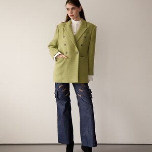 May include: A woman wearing a lime green double-breasted blazer over a white collared shirt, blue denim cargo pants with brown straps, and black heeled boots.