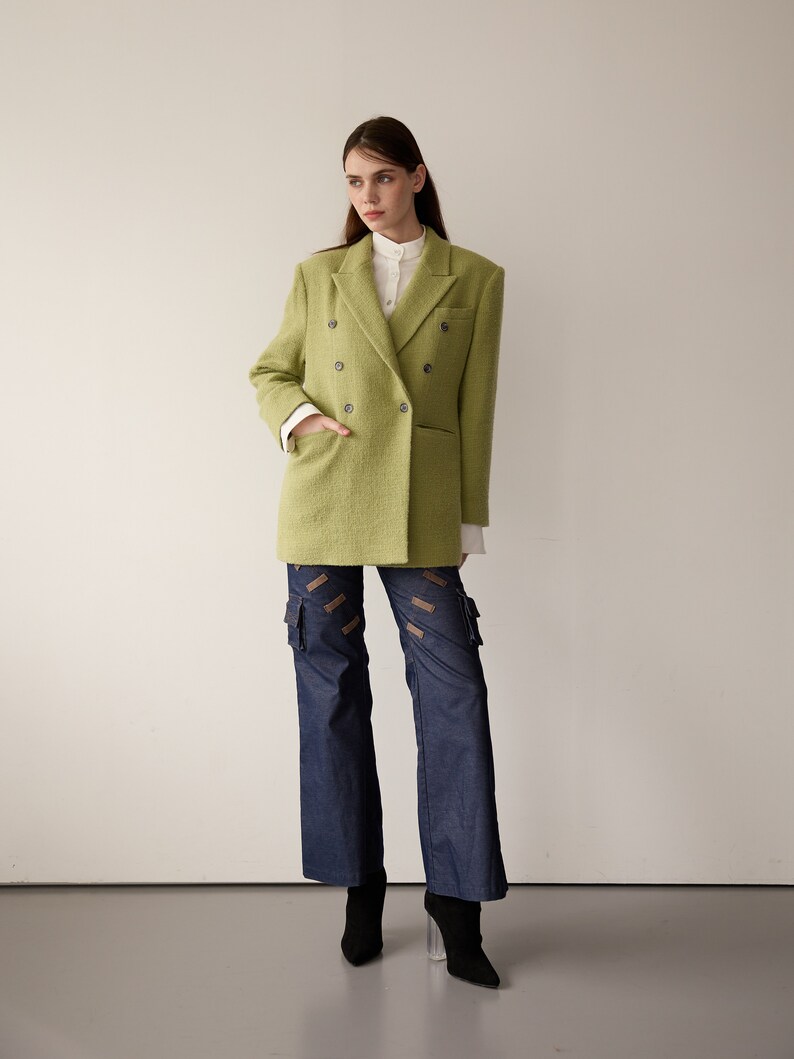 May include: A woman wearing a lime green double-breasted blazer over a white collared shirt, blue denim cargo pants with brown straps, and black heeled boots.