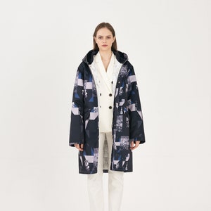 Puede incluir: Una chaqueta larga con capucha de color negro y azul con un estampado geom&eacute;trico sobre fondo blanco. Debajo lleva una camisa blanca de botones.