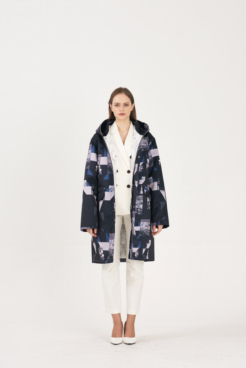 Puede incluir: Una chaqueta larga con capucha de color negro y azul con un estampado geom&eacute;trico sobre fondo blanco. Debajo lleva una camisa blanca de botones.
