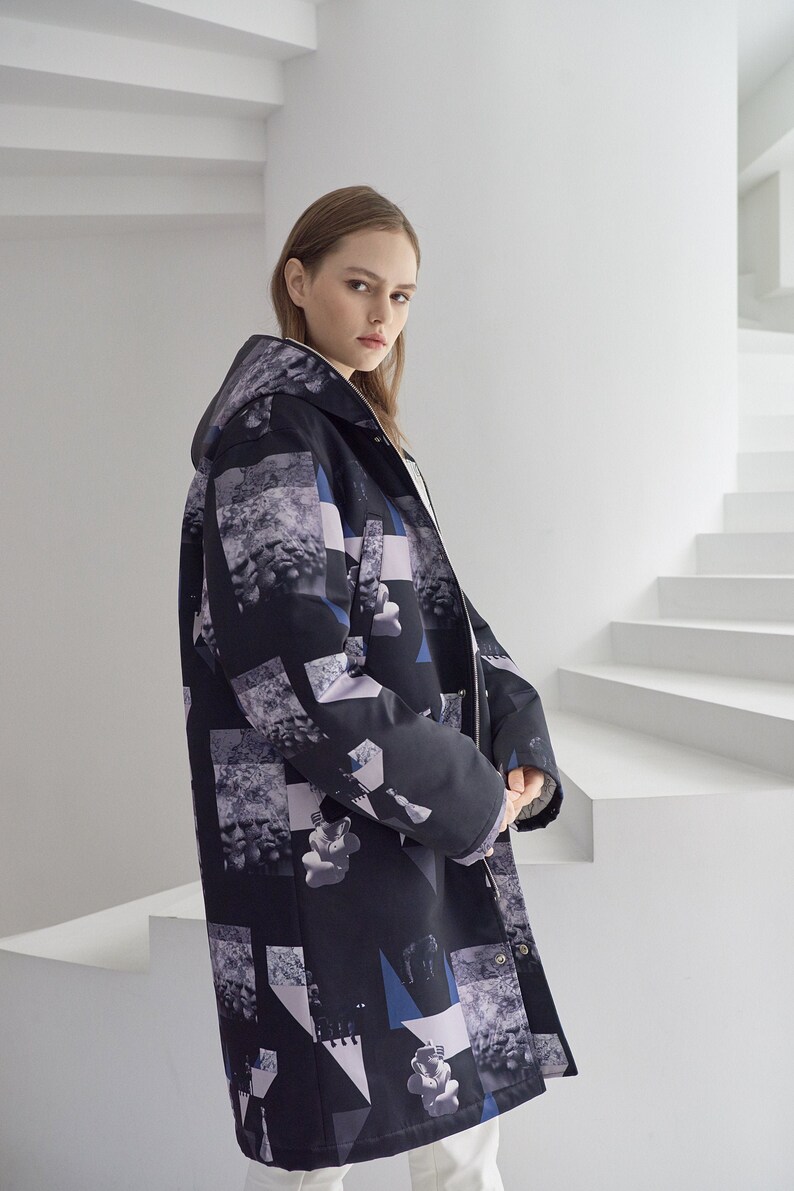 Puede incluir: Una chaqueta negra con capucha con un estampado geom&eacute;trico que presenta formas abstractas e im&aacute;genes en tonos grises, azules y blancos. La chaqueta tiene una cremallera y una capucha con cord&oacute;n.