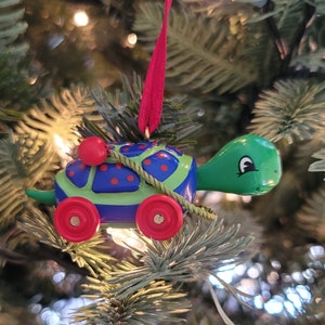 May include: A colorful turtle Christmas ornament. The turtle has a blue shell with red polka dots and green accents. It has red wheels and a red ribbon for hanging. The ornament is on a Christmas tree.