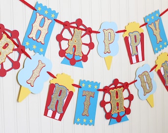 Puede incluir: Una guirnalda de Happy Birthday con temática de feria, compuesta por recortes de cartulina rojos, azules y amarillos. Las letras son de purpurina dorada y están ensartadas en una cinta roja. Incluye formas de norias, palomitas y entradas.