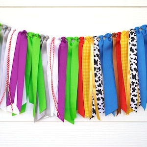 May include: A decorative ribbon garland featuring a diverse array of fabric strips in various colors including blue, green, purple, red, yellow, and pink. The collection includes solid colors, polka dots, cow print, gingham, and lace textures.