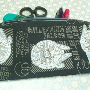May include: Black zippered pencil case with a Star Wars theme. The case features a white outline of the Millennium Falcon spaceship with the text "Millennium Falcon" and "Star Wars: The Force Awakens".