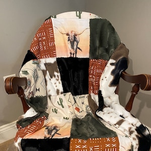 May include: A patchwork quilt with a variety of patterns and colors, including brown, black, white, and green. The quilt features a design of a longhorn steer, cacti, and geometric patterns.