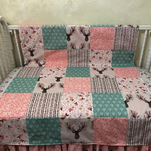 May include: A patchwork baby quilt with a pink, green, and brown color scheme. The quilt features a deer head design and floral patterns.