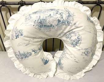 Peut inclure: Un coussin d'allaitement en forme de fer à cheval, de couleur blanche et bleue, sur le thème de Winnie l'ourson. Le coussin est orné d'un bord festonné et d'un imprimé bleu et blanc représentant Winnie l'ourson et ses amis.