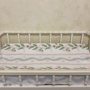 May include: White wooden changing table with a white and pink patterned changing pad. The pad has a floral design with green leaves and pink flowers.
