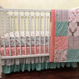 May include: A white crib with a pink and green floral patterned crib skirt and a pink and green patchwork quilt with a deer design.