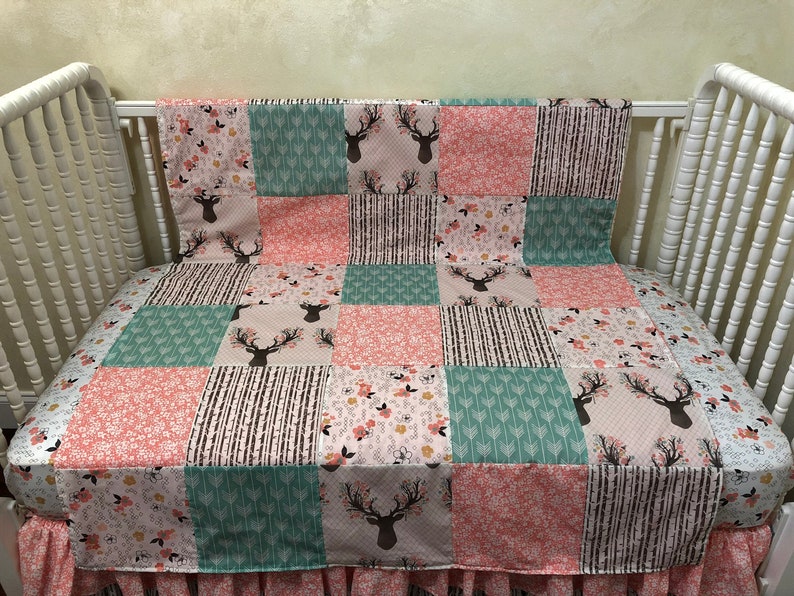 May include: A patchwork baby quilt with a pink, green, and brown color scheme. The quilt features a deer head design and floral patterns.
