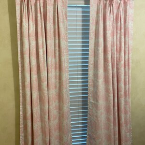 May include: A pair of pink and white patterned curtains with pleats hanging in a window with white blinds.