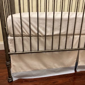 May include: A metal crib with a white fitted sheet and a white and blue ruffled crib skirt.
