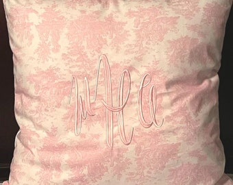 May include: A white pillow with a pink toile pattern and the monogram "M.E." embroidered in white.
