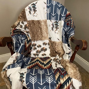 May include: A patchwork baby blanket with a variety of Native American inspired patterns, including arrows, buffalo, and geometric designs. The blanket is made of soft, plush fabric and is perfect for cuddling.