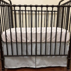 Puede incluir: Una cuna de metal marr&oacute;n oscuro con barras verticales y un colch&oacute;n blanco. La cuna tiene una falda con estampado de cuadros vichy azul claro y blanco. La cuna est&aacute; dise&ntilde;ada para un beb&eacute; o ni&ntilde;o peque&ntilde;o.