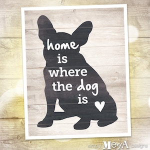 May include: Black silhouette of a French Bulldog with the text "home is where the dog is" and a small heart in the lower right corner. The background is a light wood grain.