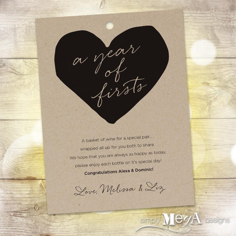 May include: A brown paper gift tag with a black heart shape and the text "a year of firsts". The tag also includes the text "A basket of wine for a special pair... wrapped all up for you both to share. We hope that you are always as happy as today, please enjoy each bottle on it's special day! Congratulations Alexa & Dominic! Love, Melissa & Liz simply Mega designs"