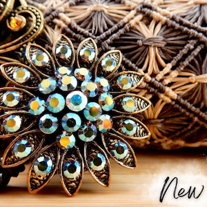 May include: A gold-toned flower-shaped badge reel with iridescent blue rhinestones. The reel is attached to a black retractable cord.