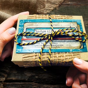A person's hands holding a small, wrapped gift box with a blue and yellow striped ribbon tied around it.