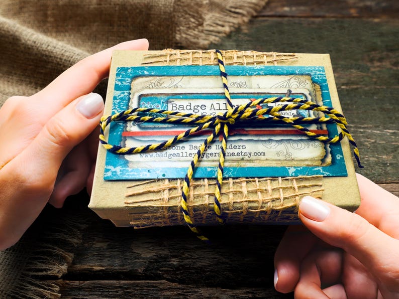 A person's hands holding a small, wrapped gift box with a blue and yellow striped ribbon tied around it.