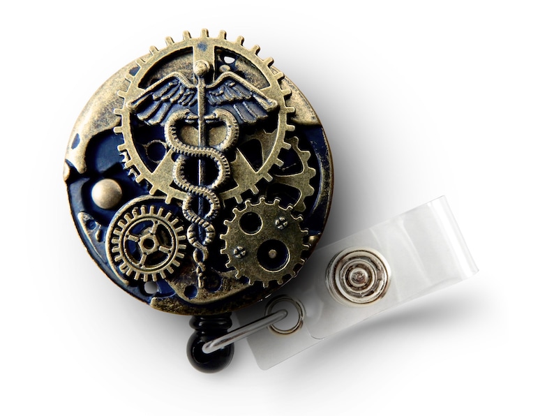 Puede incluir: Un portatarjetas de estilo steampunk con un s&iacute;mbolo m&eacute;dico de caduceo. El portatarjetas presenta una combinaci&oacute;n de colores azul y bronce con intrincados detalles de engranajes y una correa de pl&aacute;stico transparente.
